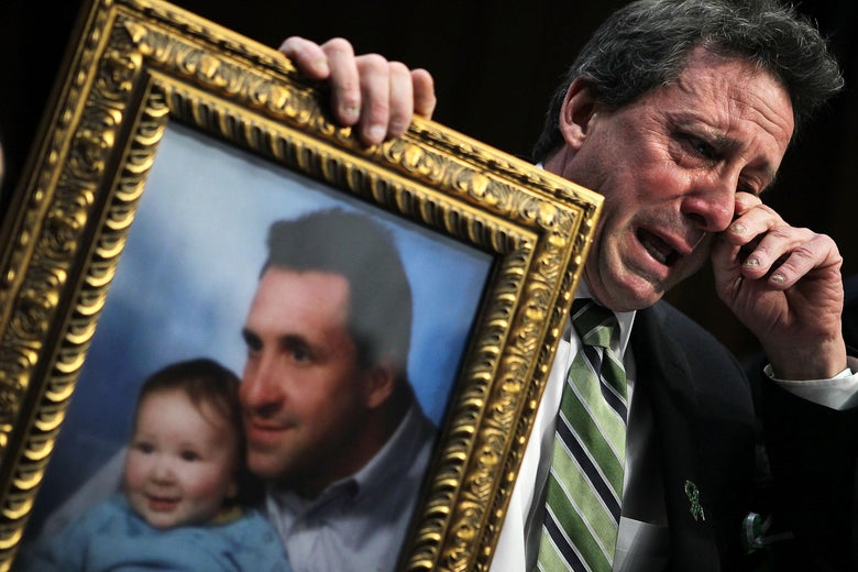 Neil Heslin wipes tears as he holds a photo of his son, Jesse Lewis, at a Senate hearing